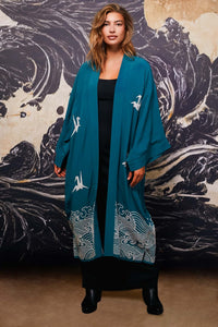 Model wears teal kimono style robe with ivory embroidery open over long black dress