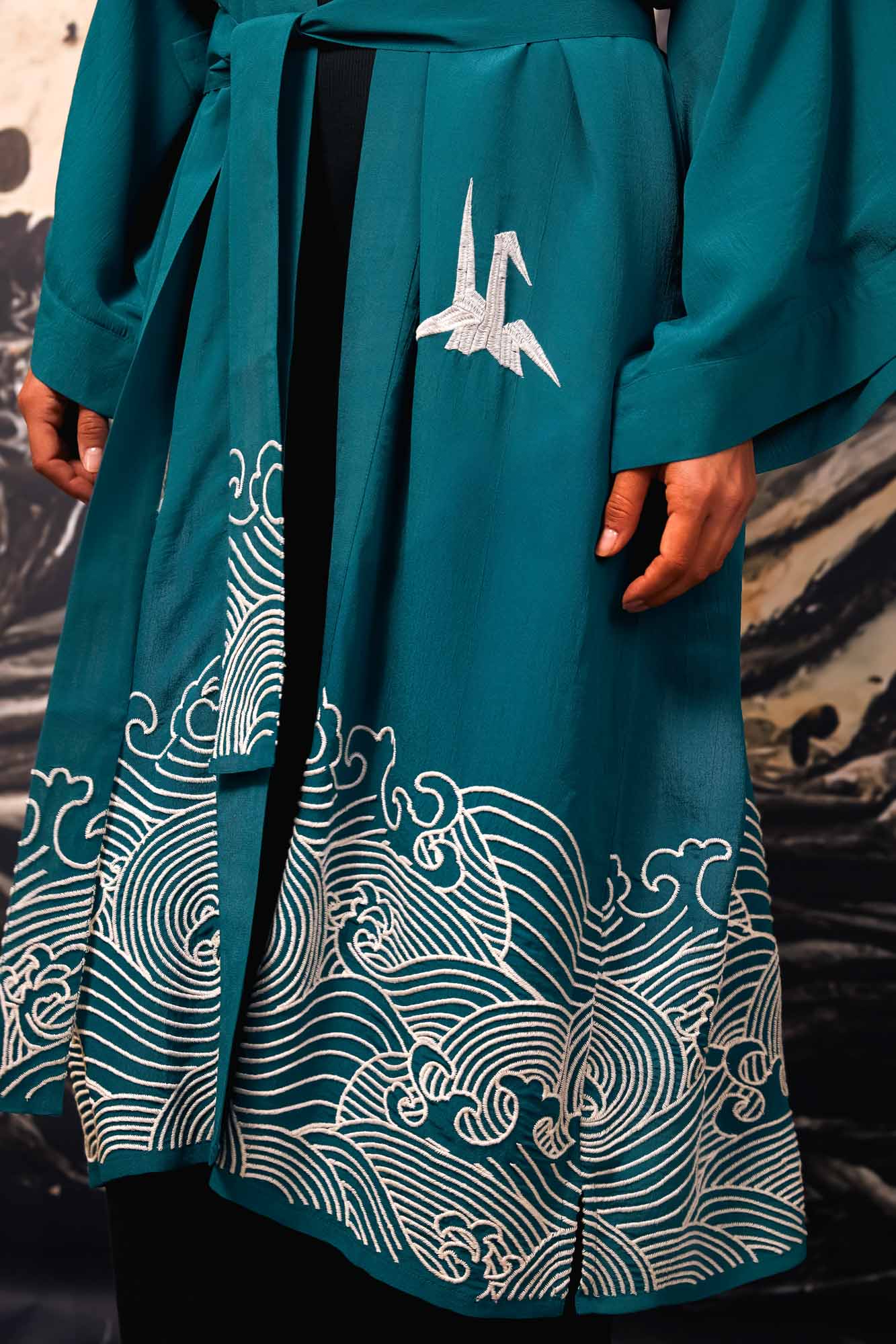 Close-up of ivory origami heron and Japanese wave embroidery adorning the bottom of teal kimono style robe