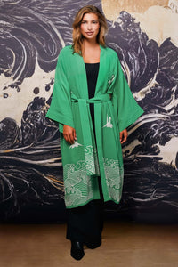 Model wears belted green kimono style robe with ivory embroidery over long black dress