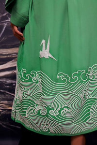 Close-up of ivory origami heron and Japanese wave embroidery adorning the bottom of green kimono style robe