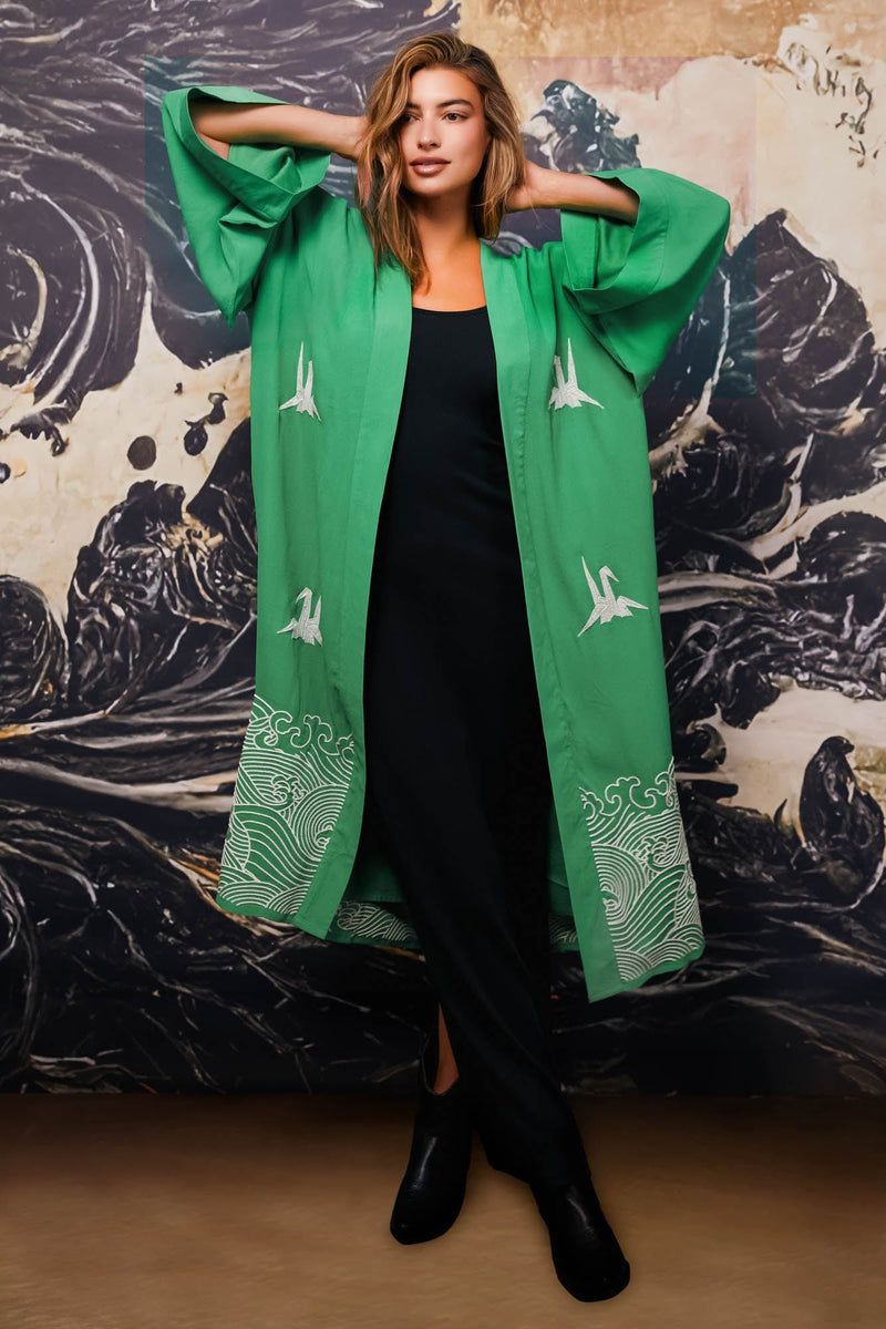 Model wears green kimono style robe with ivory embroidery open over long black dress