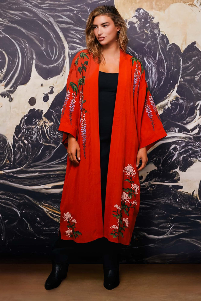 Model wears terracotta kimono style robe with wisteria and chrysanthemum embroidery open over long black dress