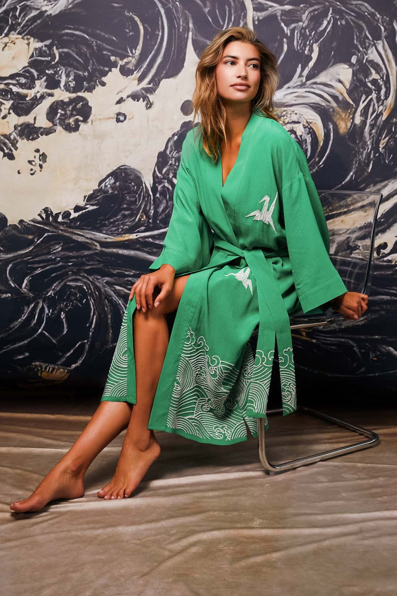 Model wears belted green kimono robe embroidered with ivory herons and waves styled over lingerie set