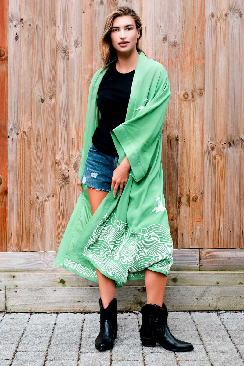 Model styles green kimono robe embroidered with ivory herons and Japanese waves over denim shorts and a black t-shirt