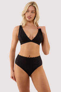 Model wears a nikki black broderie scallop high waist bikini brief with a matching bikini top.