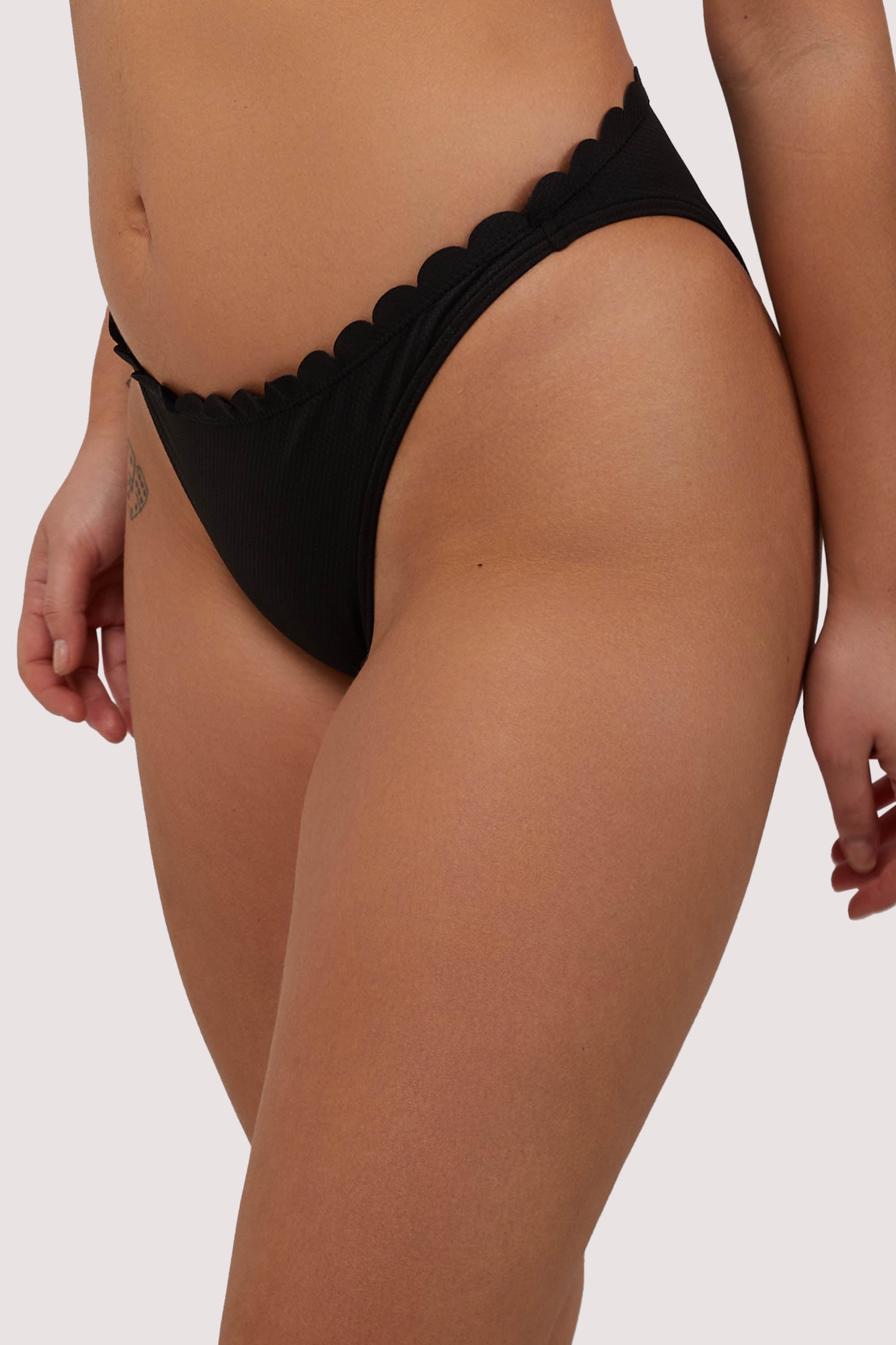 Model shows high-cut leg of sexy black scalloped bikini bottoms