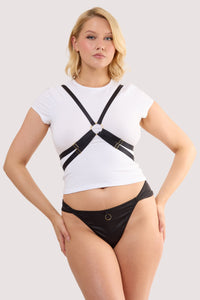 Model wears a black elastic body harness with adjustable straps and gold hardware over a white crop top.