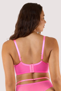 Model shows back of neon pink balconette bra with strappy details and sheer mesh panels, showcasing a bold design.