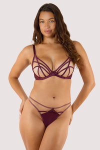 Model wears a wine thong featuring a satin central panel, strap detailing, and gold metal hardware with a matching wine plunge bra.