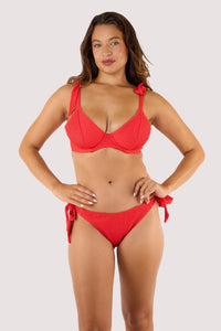model Wearing a red bikini with hands on her hips, displaying the textured fabric and supportive design of the swimwear.